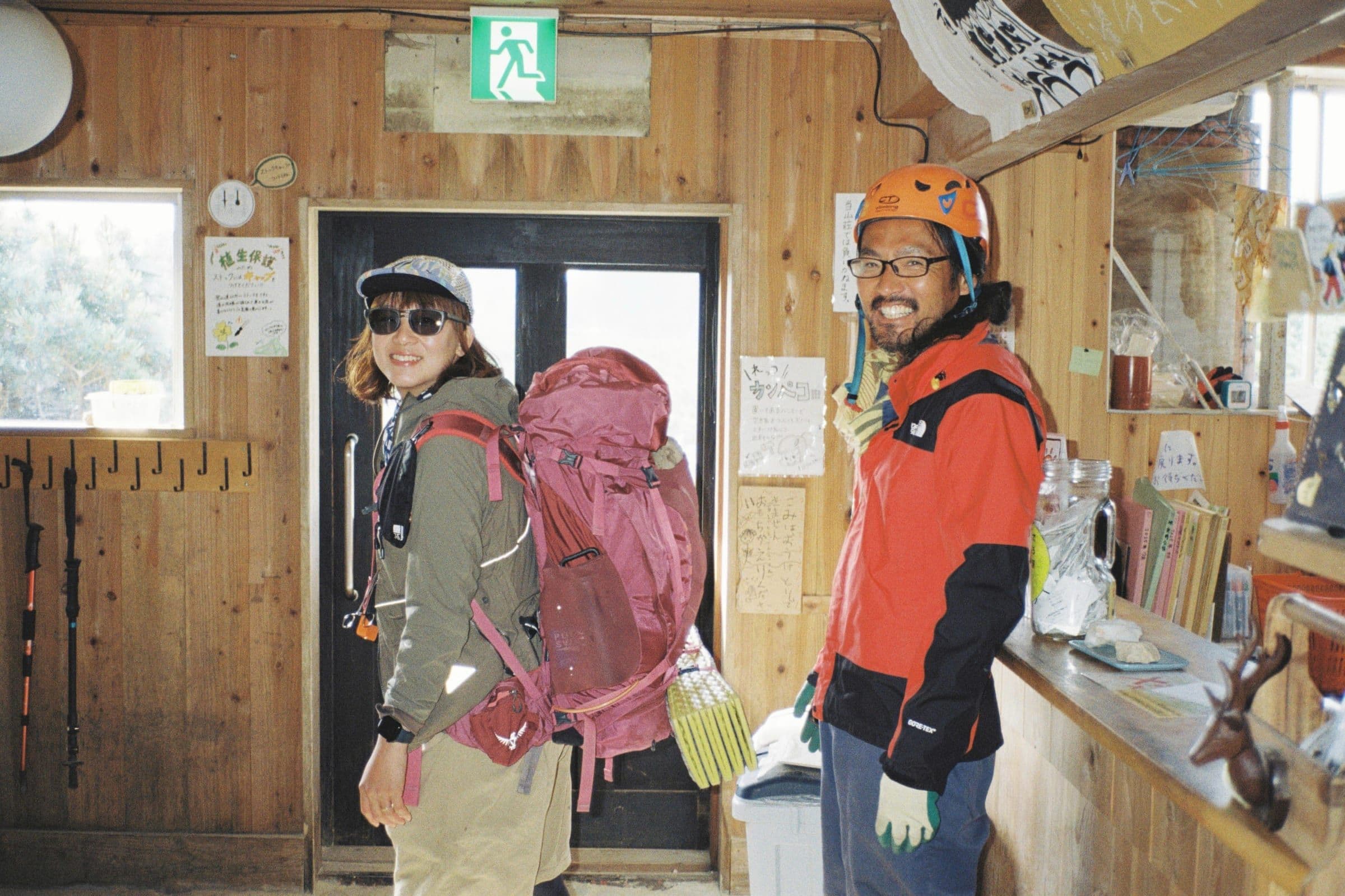 山小屋内でザックを背負うスタッフとヘルメットのスタッフ